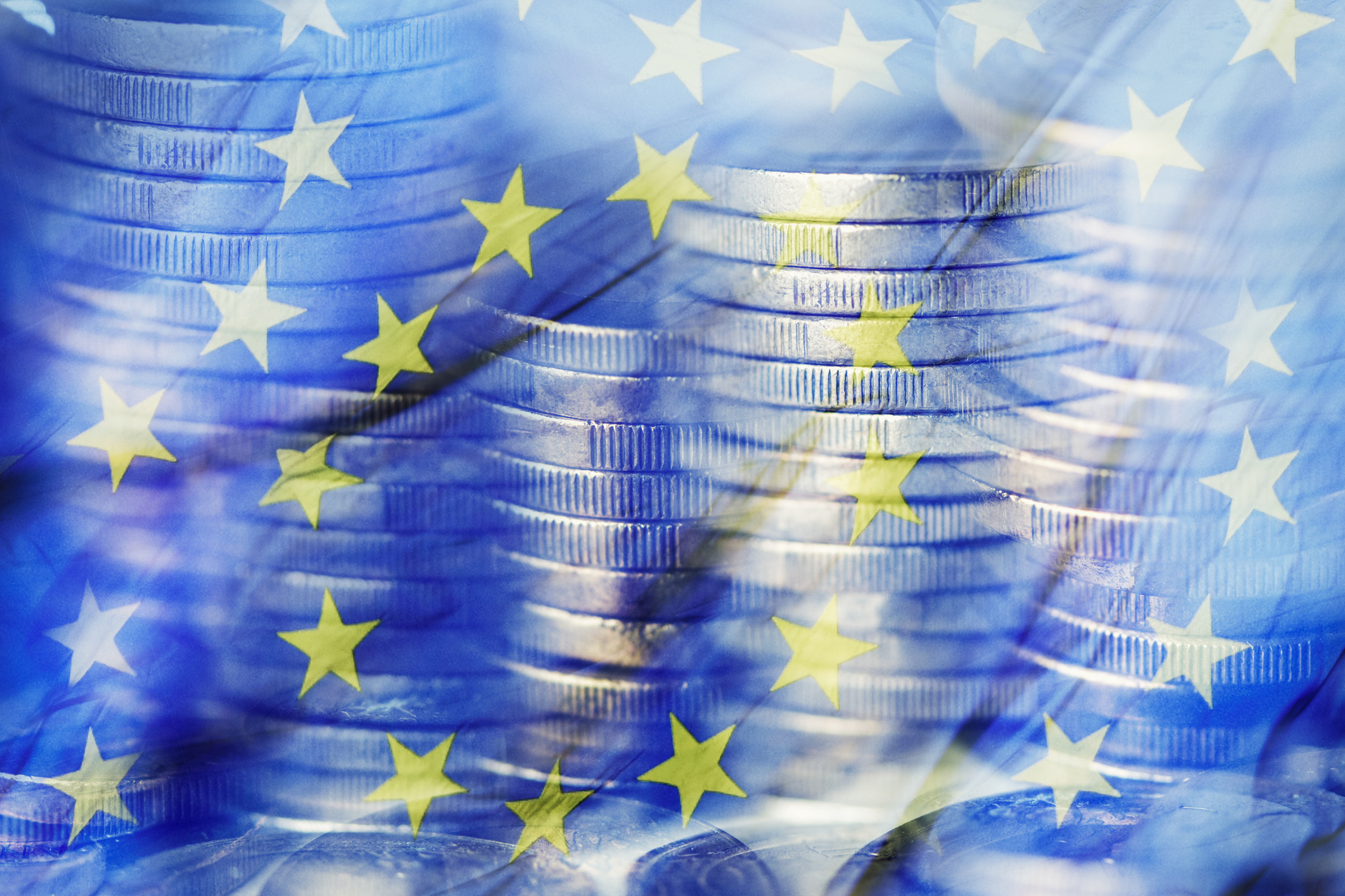 Imagen difuminada con monedas apiladas y la bandera de la Comunidad Europea