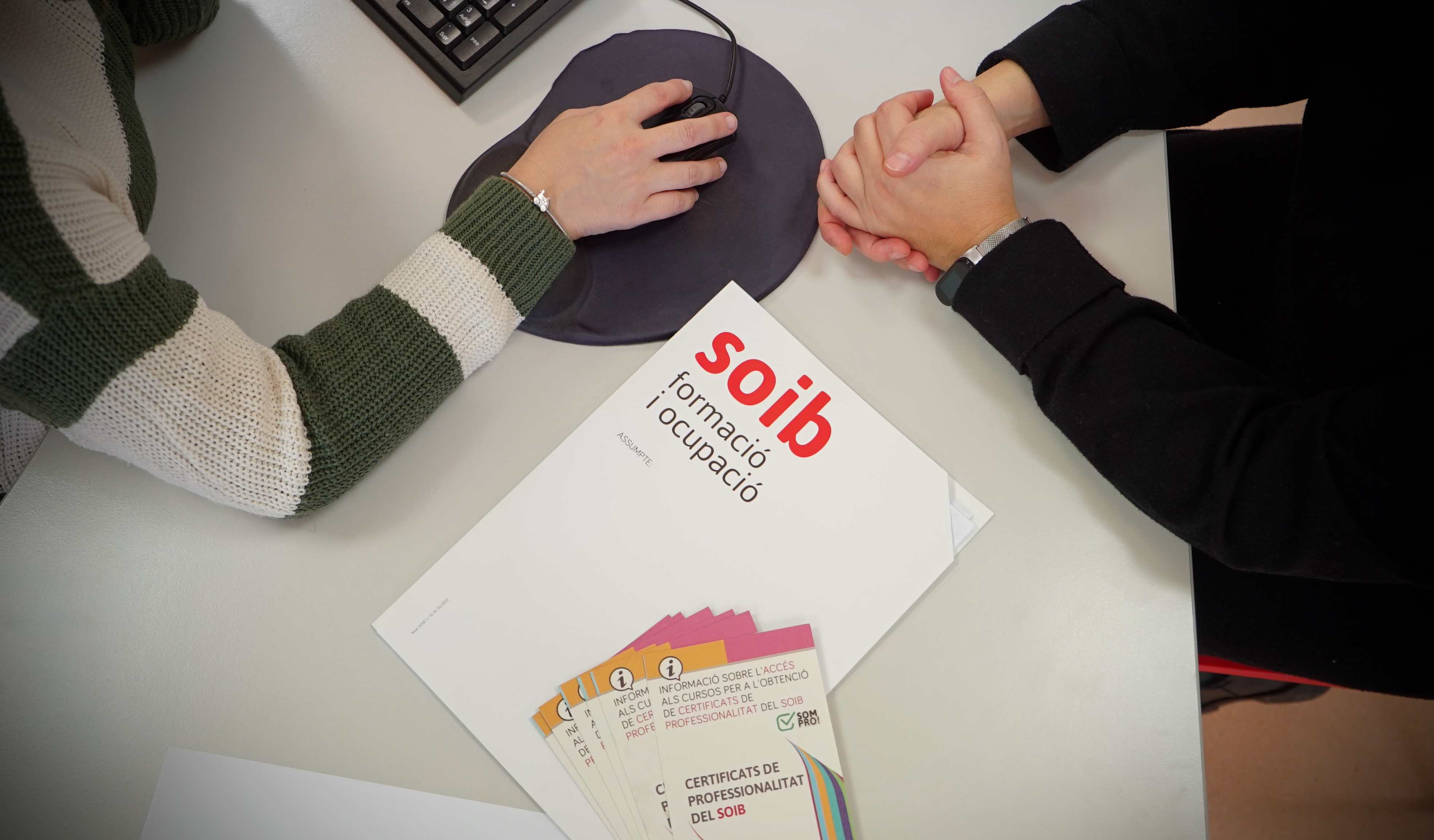 Mans damunt el ratolí d'ordinador i llibre amb el logotip del SOIB