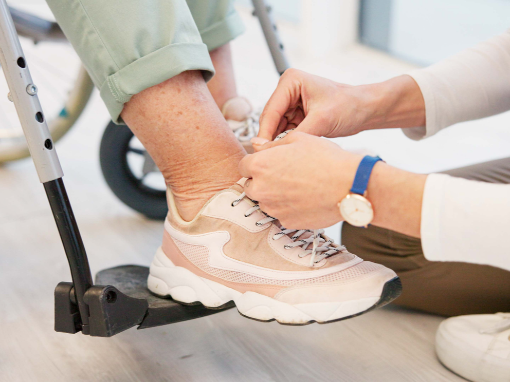 Un jove ajuda a una persona dependent a cordar-se les sabates.