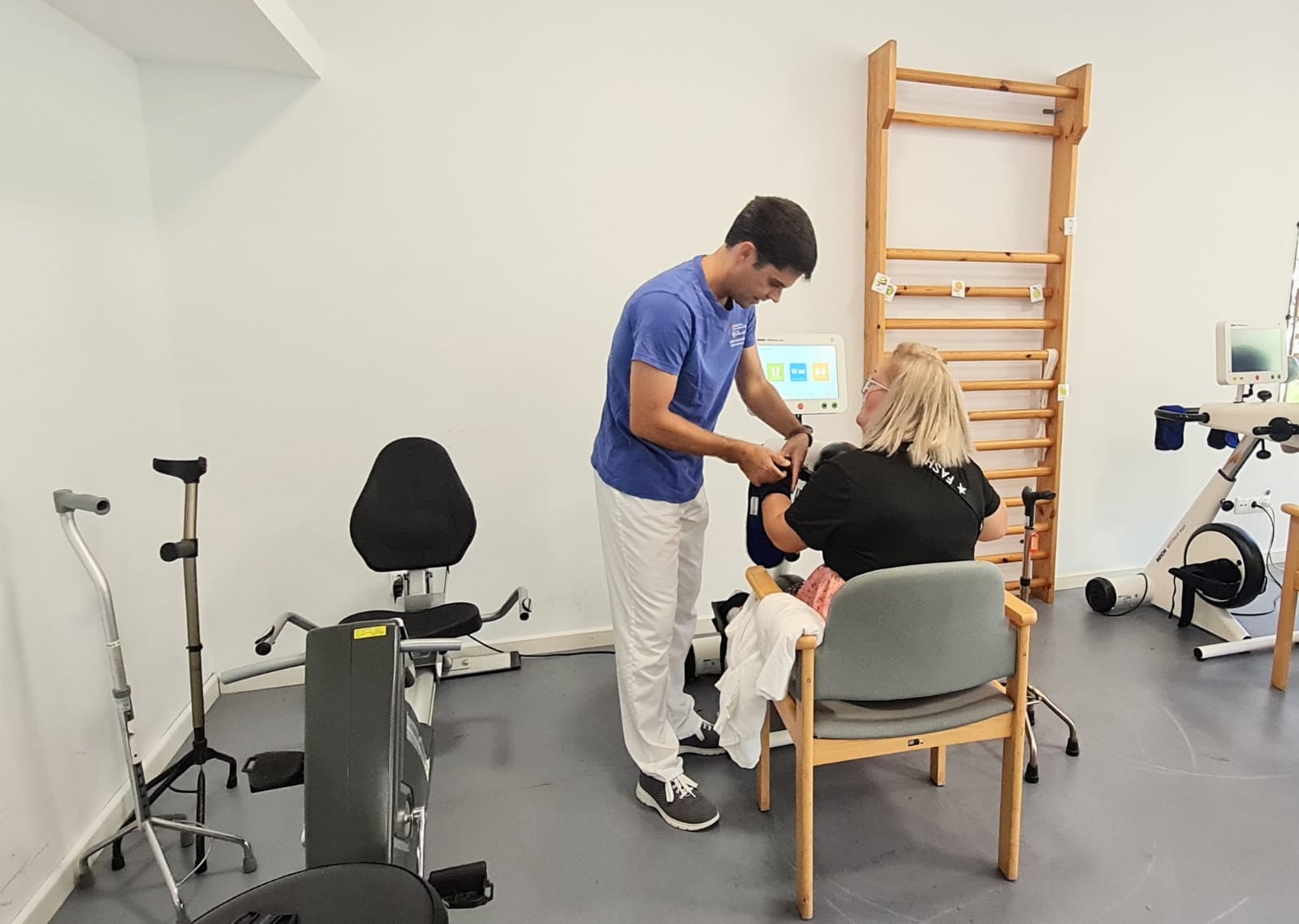 Un professional sanitari col·loca un dispositiu al braç d'una dona asseguda durant una sessió de rehabilitació.