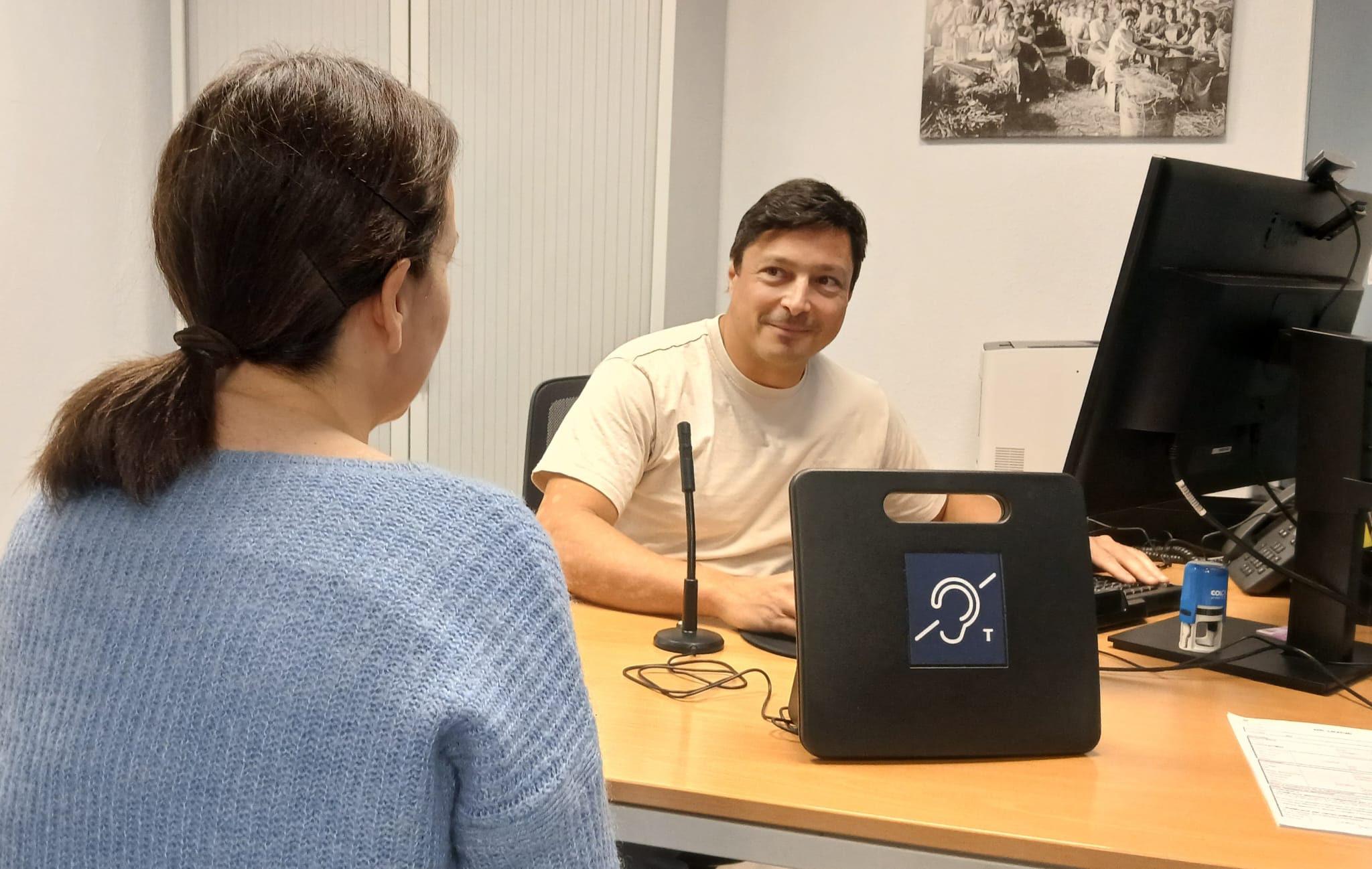 Un home atén una dona en una taula d'oficina, en la qual hi ha un bucle magnètic.