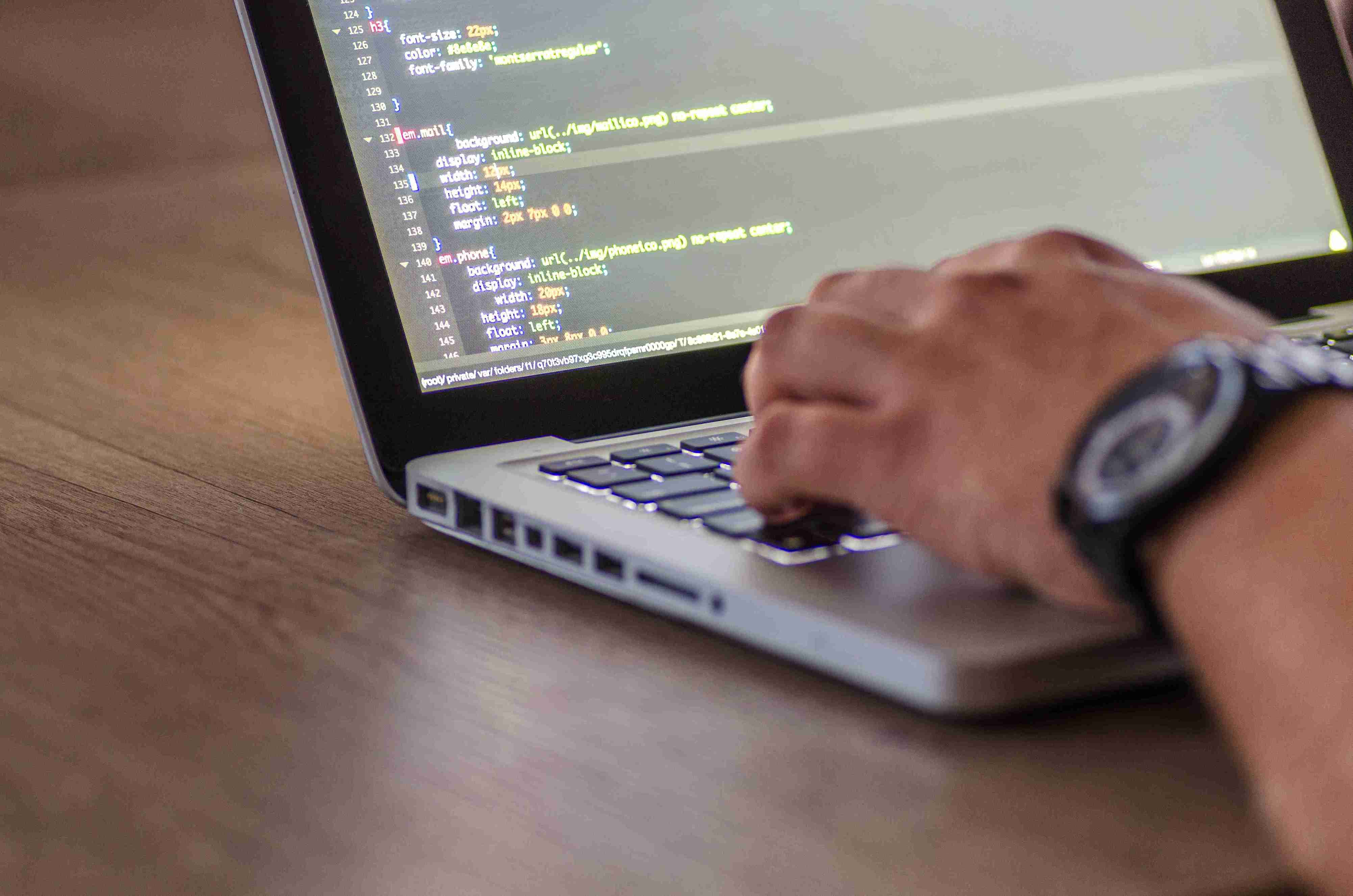 Primer pla d’una persona escrivint en un ordinador portàtil, amb codi de programació visible a la pantalla
